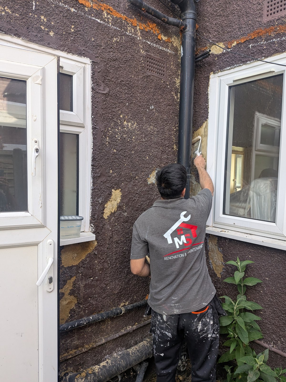 Mohamad of MS Renovation repairing an exterior wall in North London, in branded workwear