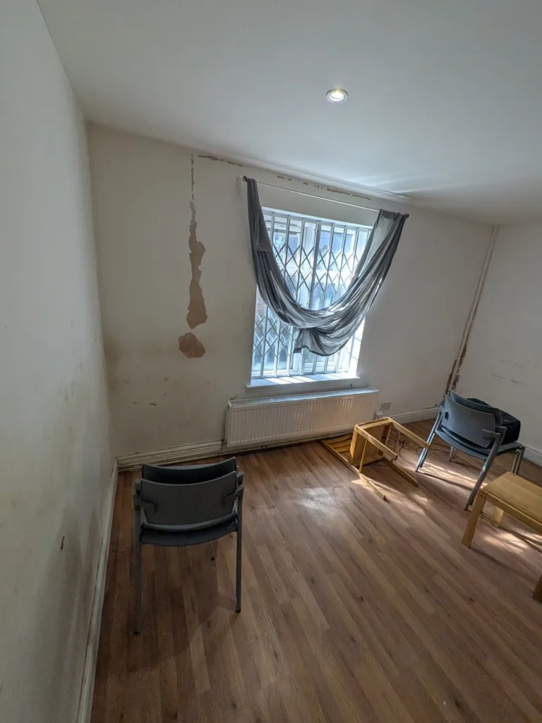 Reception room in Harlesden NW10 with damp staining beside a barred window, before repair